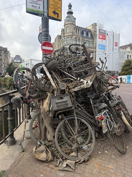 This photo captures a striking scene on Singel, Centrum, Amsterdam, featuring a massive pile of discarded bicycles next to a canal